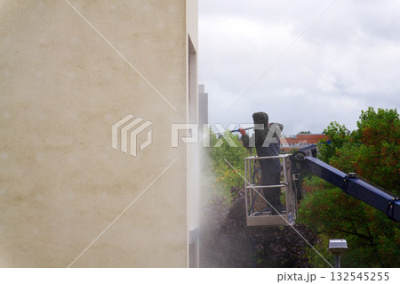 Unrecognizable man cleaning facade surface from lifting platform with high pressure stream of water 132545255