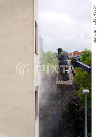 Unrecognizable man cleaning facade surface from lifting platform with high pressure stream of water 132545257