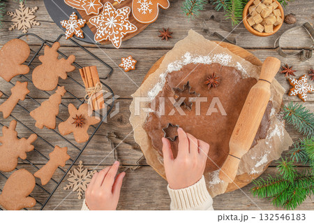 Christmas cookie making process with hands cutting shapes from gingerbread dough using cutters on rustic wooden table, holiday baking concept, spices, and decorated cookies, top view copy space 132546183