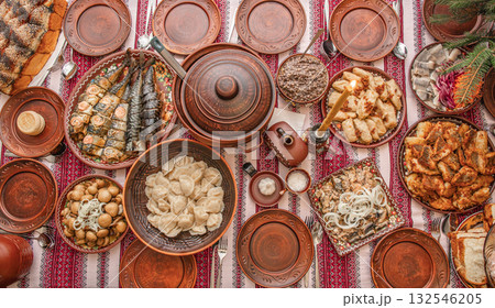 Traditional Ukrainian Christmas Eve dinner table with kutia, varenyky, stuffed cabbage rolls, fried fish, festive dishes served in bowls on embroidered rushnyk, authentic Sviat Vechir meal top view 132546205