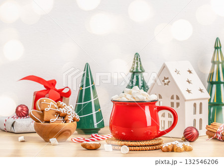 Red mug of hot chocolate marshmallows gingerbread cookies, festive Christmas scene with ceramic trees, gift, candy canes house lantern on light background, holiday composition copy space Red mug of hot chocolate marshmallows gingerbread cookies, festive Christmas scene with ceramic trees, gift, candy canes house lantern on light background, holiday composition copy space 132546206