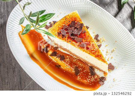 Slice of caramel cheesecake with chocolate flakes and sauce garnish served on a white plate 132546292