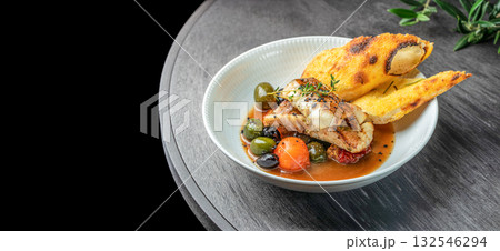 Grilled fish fillet served with olives, cherry tomatoes, and sauce accompanied by crispy focaccia bread on a white plate. top view. copy space. Grilled fish fillet served with olives, cherry tomatoes, and sauce accompanied by crispy focaccia bread on a white plate. top view. copy space. 132546294