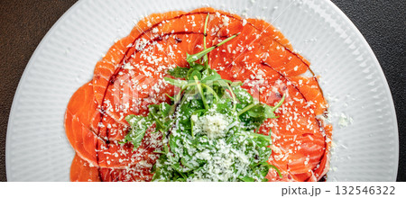 Top view of salmon carpaccio garnished with arugula, grated cheese, and balsamic glaze on a white plate Top view of salmon carpaccio garnished with arugula, grated cheese, and balsamic glaze on a white plate 132546322