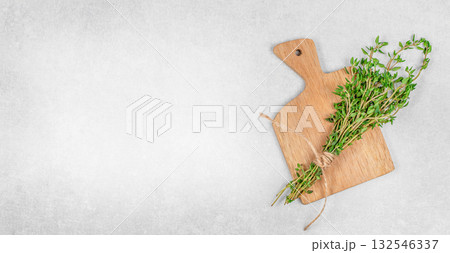 Fresh thyme bunch tied with rope on wooden cutting board over gray stone background with copy space. Organic herbs for cooking, natural seasoning, food template design Fresh thyme bunch tied with rope on wooden cutting board over gray stone background with copy space. Organic herbs for cooking, natural seasoning, food template design 132546337