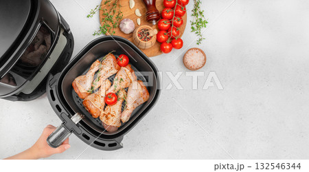 Raw chicken drumsticks with tomatoes and herbs in air fryer basket, preparation for healthy cooking at home, modern kitchen appliance top view with copy space Raw chicken drumsticks with tomatoes and herbs in air fryer basket, preparation for healthy cooking at home, modern kitchen appliance top view with copy space 132546344