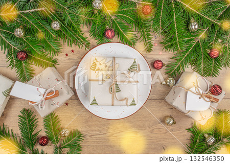 Christmas composition with gift box on a plate surrounded by fir branches and festive decorations on wooden table, holiday background with copy space for celebration Christmas composition with gift box on a plate surrounded by fir branches and festive decorations on wooden table, holiday background with copy space for celebration 132546350