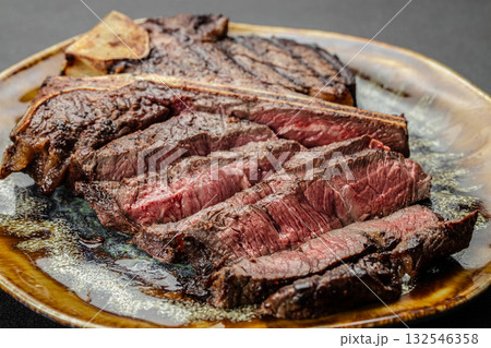 Close up of juicy grilled beef steak T-bone sliced medium rare and served on a ceramic plate. Perfect gourmet meat dish for steakhouse, barbecue, restaurant menu, or culinary advertising Close up of juicy grilled beef steak T-bone sliced medium rare and served on a ceramic plate. Perfect gourmet meat dish for steakhouse, barbecue, restaurant menu, or culinary advertising 132546358