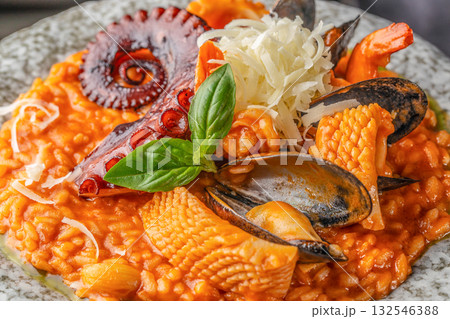 Delicious Italian risotto served with octopus tentacle, mussels, squid, shrimp, tomato sauce and grated parmesan cheese, garnished with fresh basil Delicious Italian risotto served with octopus tentacle, mussels, squid, shrimp, tomato sauce and grated parmesan cheese, garnished with fresh basil 132546388