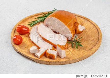 Juicy smoked chicken breast sliced and served on a wooden cutting board with rosemary and fresh tomatoes, delicious lean meat delicacy, rustic culinary presentation on light background 132546401