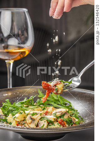 Close-up of gnocchi pasta with mushrooms, arugula, sun-dried tomatoes, and parmesan cheese being sprinkled by hand 132546420