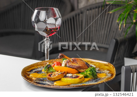 Gourmet roasted duck leg served with grilled vegetables, broccoli, sauce, and a glass of red wine on the table 132546421