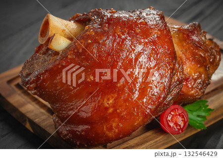 roasted pork knuckle with crispy glazed skin, served with cherry tomato and parsley on a wooden board 132546429