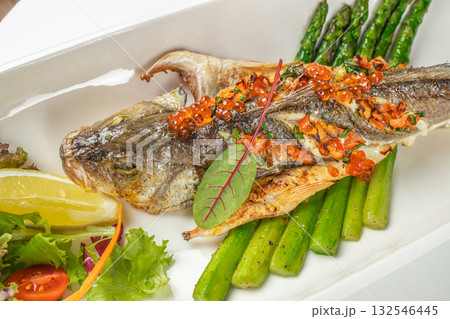 Whole grilled seabass served with asparagus, salmon roe, lemon, and fresh salad garnish Whole grilled seabass served with asparagus, salmon roe, lemon, and fresh salad garnish 132546445