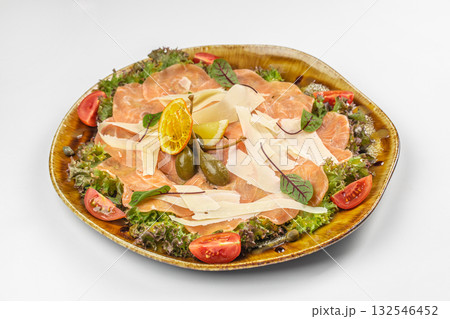 Plate of salmon carpaccio served with parmesan shavings, capers, lemon, tomato, and fresh greens 132546452