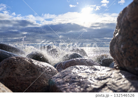 Sea waves breaking on rocks with sunlight reflection and cloudy horizon. 132546526