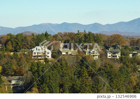 View from above of expensive residential houses high on hill top between yellow fall trees in suburban area in North Carolina. American dream homes as example of real estate development in US suburbs View from above of expensive residential houses high on hill top between yellow fall trees in suburban area in North Carolina. American dream homes as example of real estate development in US suburbs 132546906