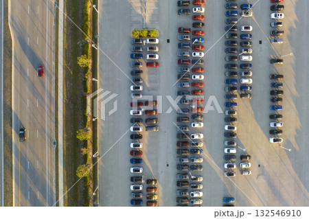 View from above of dealers outdoor parking lot with many brand new cars in stock for sale on highway side. Concept of development of american automotive industry View from above of dealers outdoor parking lot with many brand new cars in stock for sale on highway side. Concept of development of american automotive industry 132546910