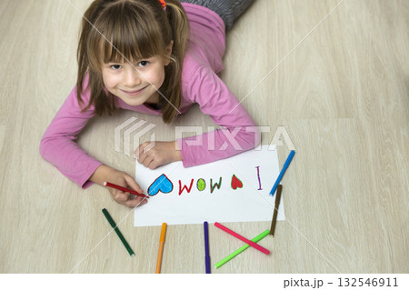 View from above of cute child girl drawing with colorful crayons I love Mom on white paper. Art education, creativity concept. 132546911