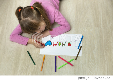 View from above of cute child girl drawing with colorful crayons I love Mom on white paper. Art education, creativity concept. 132546922