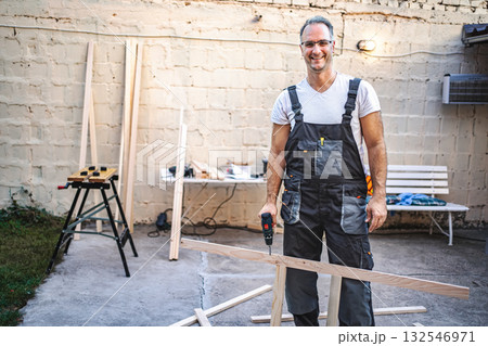 Mature male carpenter using electric screwdriver on a wooden plank outdoors Mature male carpenter using electric screwdriver on a wooden plank outdoors 132546971