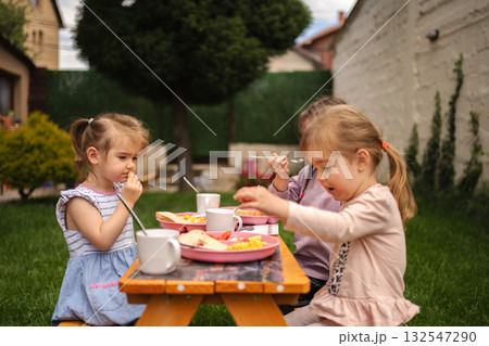 Young children enjoying a delightful outdoor meal in bright sunshine Young children enjoying a delightful outdoor meal in bright sunshine 132547290