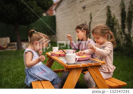Children enjoying a sunny day at a picnic table in the garden Children enjoying a sunny day at a picnic table in the garden 132547291