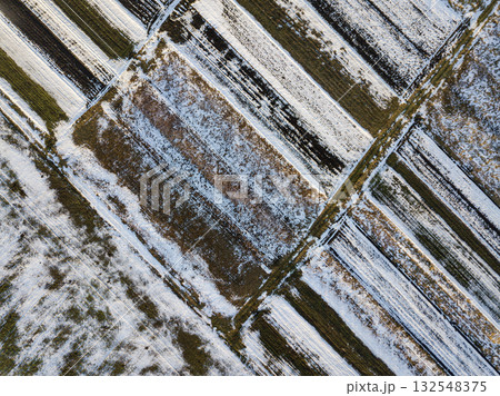 Top view of empty snowy and dark fields patched landscape on sunny winter day. Aerial drone photography concept. Top view of empty snowy and dark fields patched landscape on sunny winter day. Aerial drone photography concept. 132548375