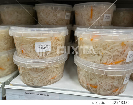 Containers of fermented cabbage with carrots displayed on a shelf, showcasing traditional food preservation methods and vibrant colors in a grocery store environment 132548380