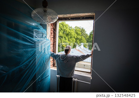 Renovation contemplation, woman surveys ongoing window renovation activities from window overlooking leafy street Renovation contemplation, woman surveys ongoing window renovation activities from window overlooking leafy street 132548425