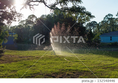 Sprinkler watering lawn grass during dry season Sprinkler watering lawn grass during dry season 132548446