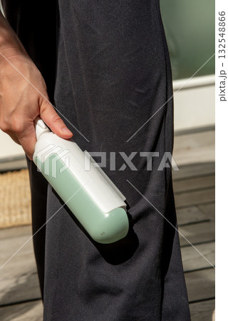 Woman using reusable clothes lint roller cleaner. Close up of woman removing dog hair from clothing Woman using reusable clothes lint roller cleaner. Close up of woman removing dog hair from clothing 132548866