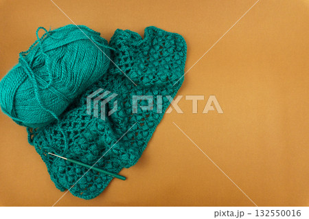 Teal crocheted item made with merino wool yarn and crochet hook on warm background, flat lay with copy space for craft tutorials and knitting inspiration Teal crocheted item made with merino wool yarn and crochet hook on warm background, flat lay with copy space for craft tutorials and knitting inspiration 132550016