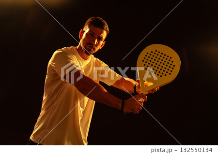 Man practicing paddle tennis with a strong stance in a dark setting Man practicing paddle tennis with a strong stance in a dark setting 132550134