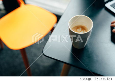 Coffee cup on a black table with an orange chair in a cozy workspace Coffee cup on a black table with an orange chair in a cozy workspace 132550184