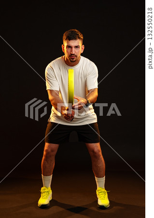 Man preparing to strike with a racket in a dark studio setting, highlighting athletic focus Man preparing to strike with a racket in a dark studio setting, highlighting athletic focus 132550218