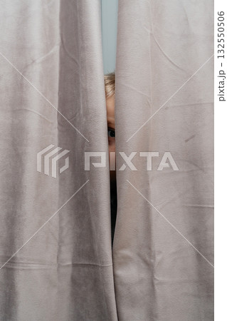 Narrow vertical slice shows a childs eye peeking between gray curtains intimate, mysterious home detail Narrow vertical slice shows a childs eye peeking between gray curtains intimate, mysterious home detail 132550506