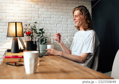 Young man enjoying a cozy workspace with a warm drink and plants in a bright room Young man enjoying a cozy workspace with a warm drink and plants in a bright room 132550649