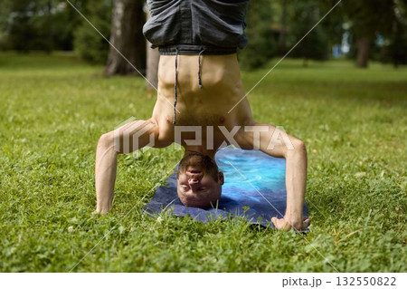 A person performing an impressive handstand yoga pose on the lush green grass outdoors 132550822