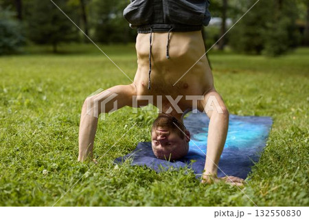 Practicing the Upside Down Yoga Pose on a Mat in a Beautiful Green Park Among Nature Practicing the Upside Down Yoga Pose on a Mat in a Beautiful Green Park Among Nature 132550830