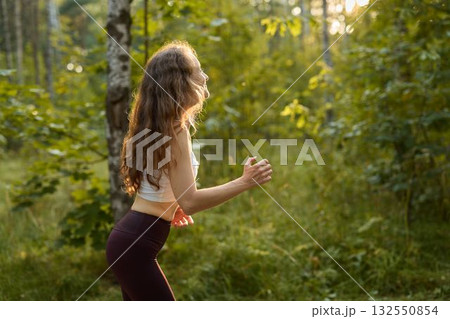 An Energetic Woman Joyfully Running Through a Lush Green and Vibrant Forest Environment 132550854