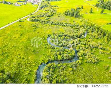 A tranquil river winds gracefully through a verdant valley, surrounded by lush greenery and dotted with trees. The stunning alpine landscape reveals nature's beauty from above. A tranquil river winds gracefully through a verdant valley, surrounded by lush greenery and dotted with trees. The stunning alpine landscape reveals nature's beauty from above. 132550966