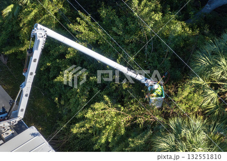 Maintenance of electrical grid by city utility cervices. Worker in lift truck trimming tree around power lines Maintenance of electrical grid by city utility cervices. Worker in lift truck trimming tree around power lines 132551810