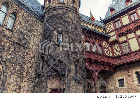 Old castle in Wernigerode covered with dry ivy and gothic details creates a moody mysterious scene. Weathered walls and carved wooden balcony evoke legends and haunting medieval charm Old castle in Wernigerode covered with dry ivy and gothic details creates a moody mysterious scene. Weathered walls and carved wooden balcony evoke legends and haunting medieval charm 132551947