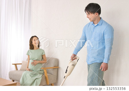 妊婦の女性と話しながら楽しそうに掃除機をかける若い男性 132553356