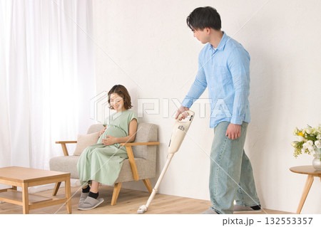 妊婦の女性と話しながら楽しそうに掃除機をかける若い男性 妊婦の女性と話しながら楽しそうに掃除機をかける若い男性 132553357