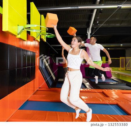 Cheerful girl throwing foam cube into basketball hoop in trampoline park 132553380