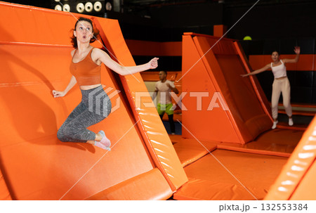 Cheerful woman pushing off sloped trampoline in indoor playground 132553384