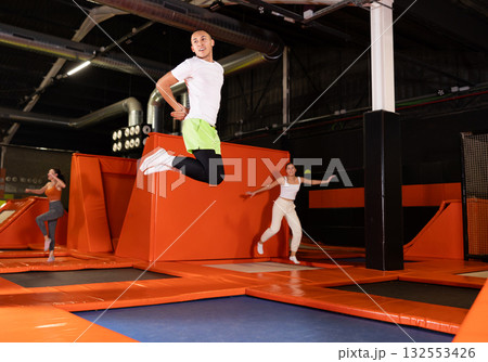 Cheerful young man jumping in modern indoor trampoline park Cheerful young man jumping in modern indoor trampoline park 132553426