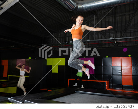 Enthusiastic woman leaping at vibrant trampoline gym with friends 132553437